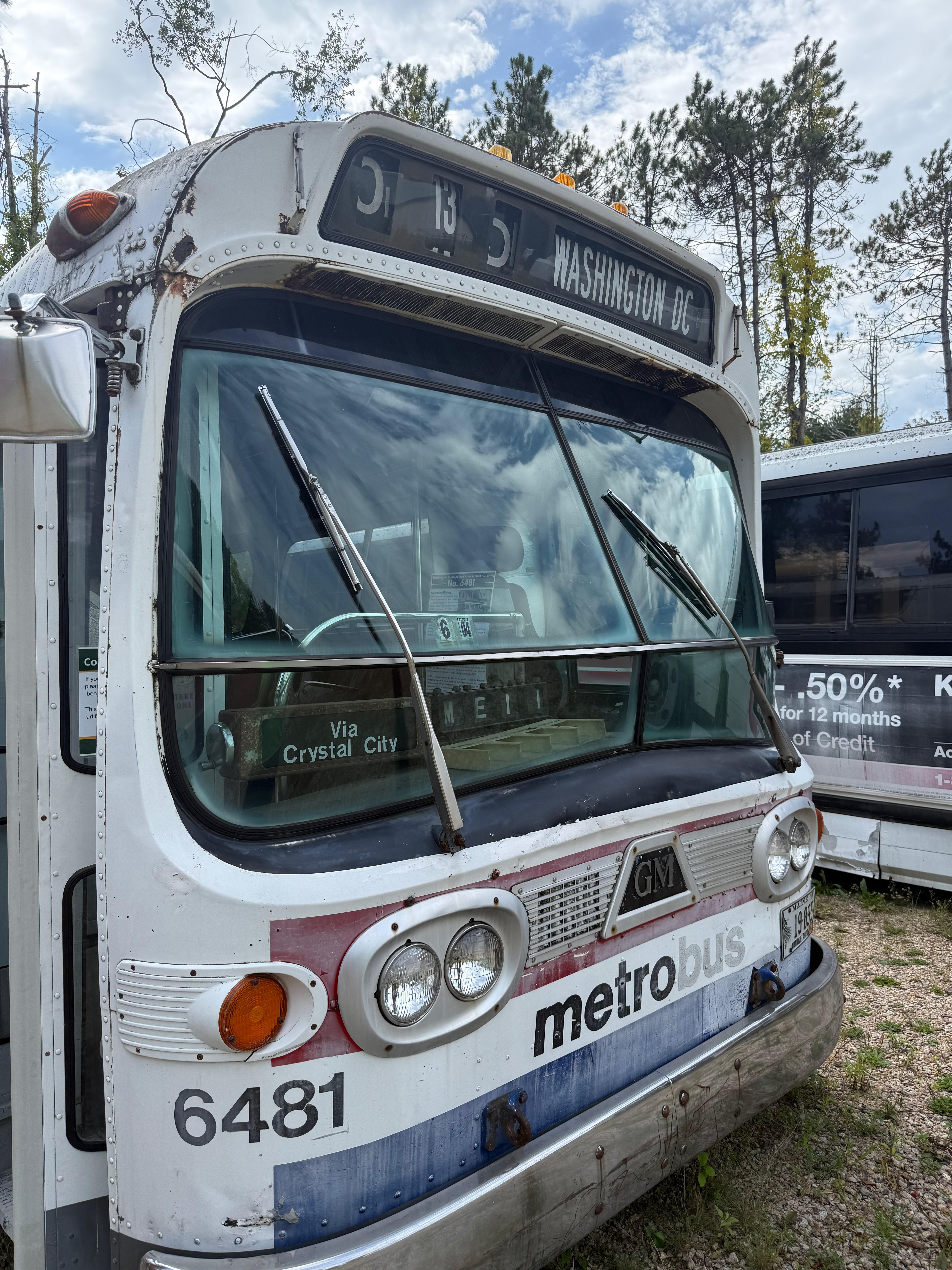 A close-up of the front of a weathered, white GM “metrobus” from Washington D.C. The destination sign reads “WASHINGTON DC” and “Via Crystal City”. The bus, number 6481, shows signs of aging.